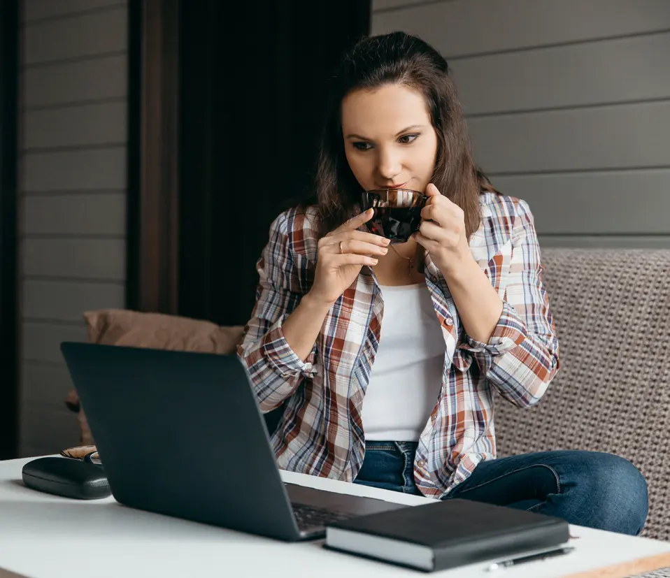 a woman sitting at a table with a laptop and a cup of coffee.