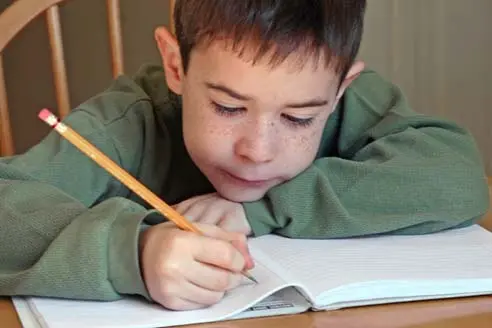 a young boy writing on a book with a pencil.