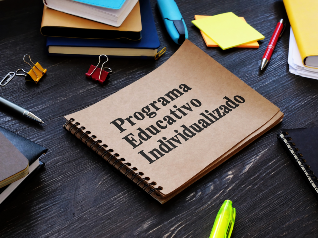 Brown spiral notebook labeled "Programa Educativo Individualizado" on a dark wooden desk among colorful stationery.