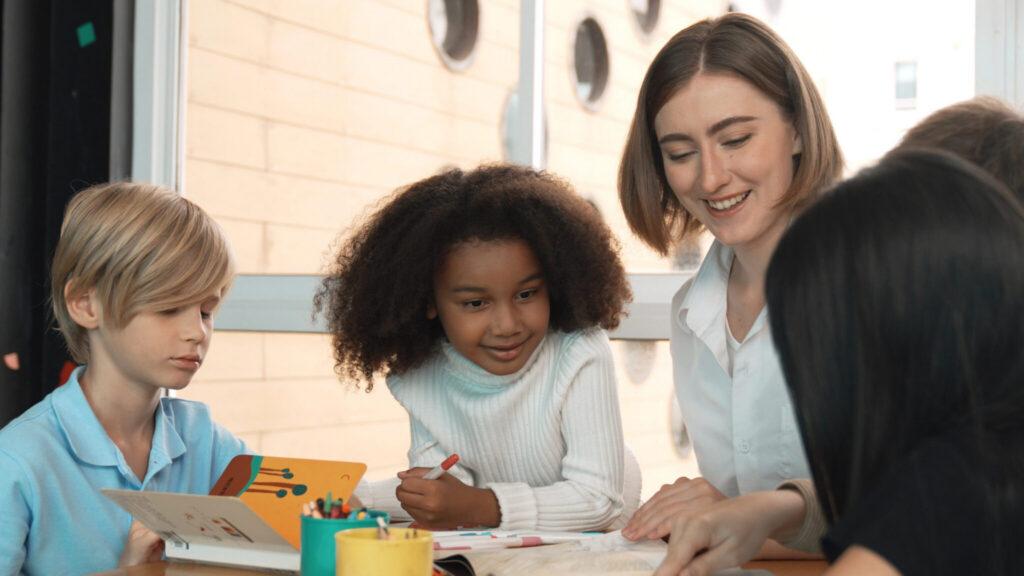 A teacher and three students work on an art project together at a classroom table.